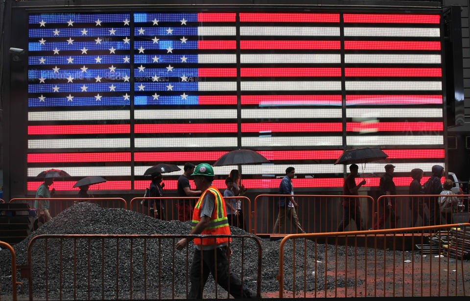 NEW YORK, NY - AUGUST 22: Pedestrians and a construction worker walk past a lit American flag in the rain in Times Square on August 22, 2013 in New York City.  The afternoon rain that fell in the city today is expected to clear up mostly by tomorrow.  (Photo by Mario Tama/Getty Images)